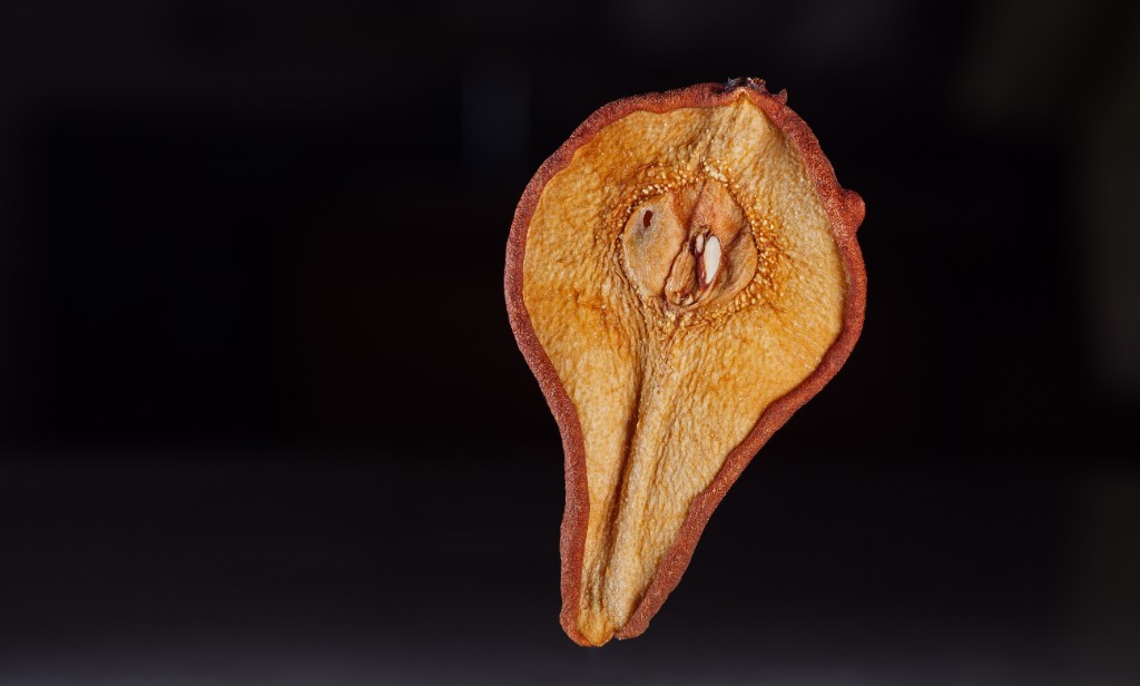A dried pear slice in warm golden-brown tones against a dark background