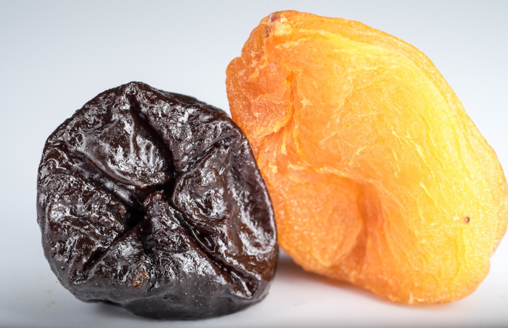 Close-up of a glossy dried prune and a bright dried apricot on a white background